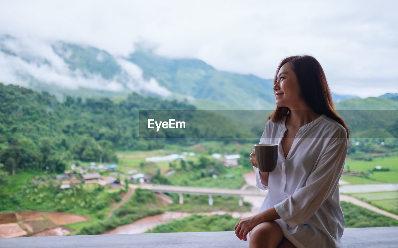 Young woman with coffee cup sitting against mountains