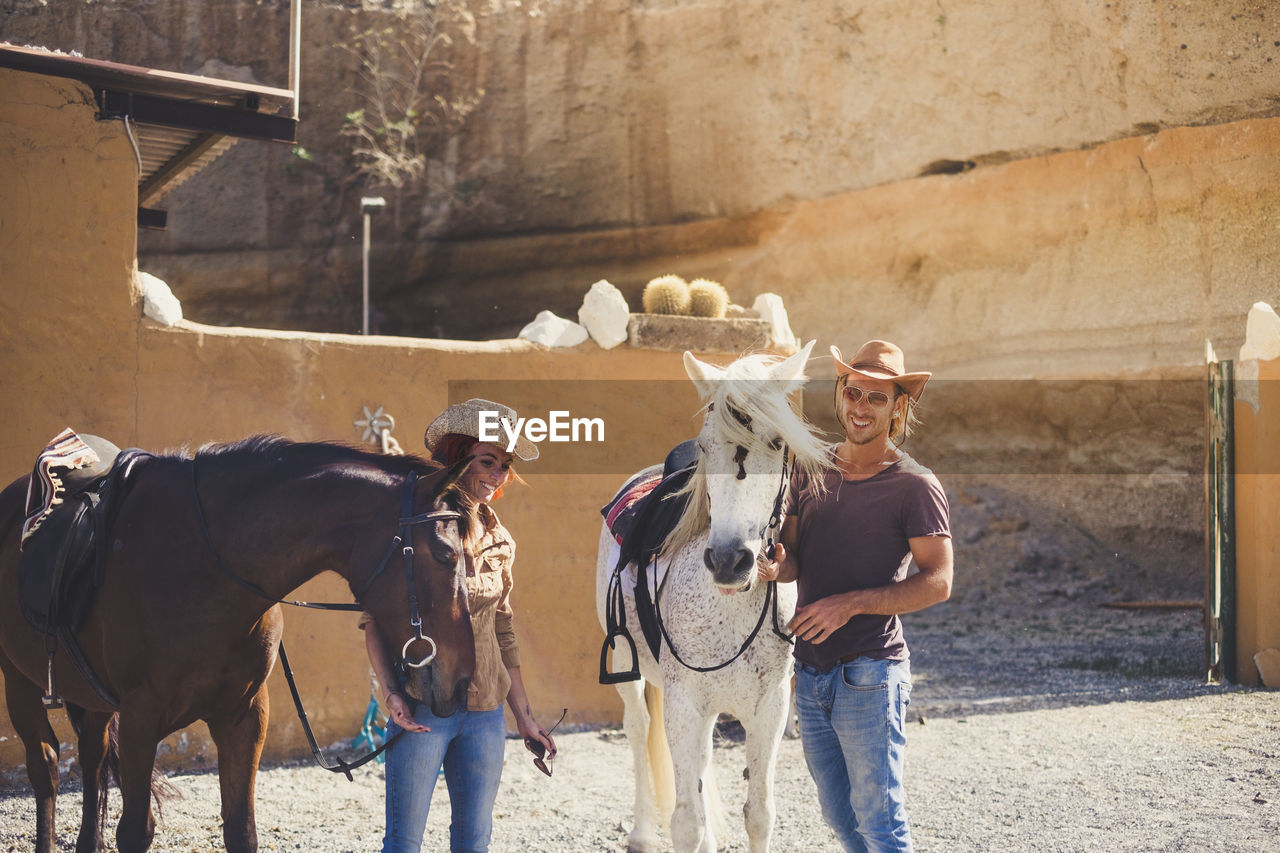 Friends standing with horses on field