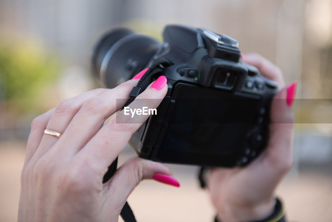 Cropped hand holding camera while standing outdoors