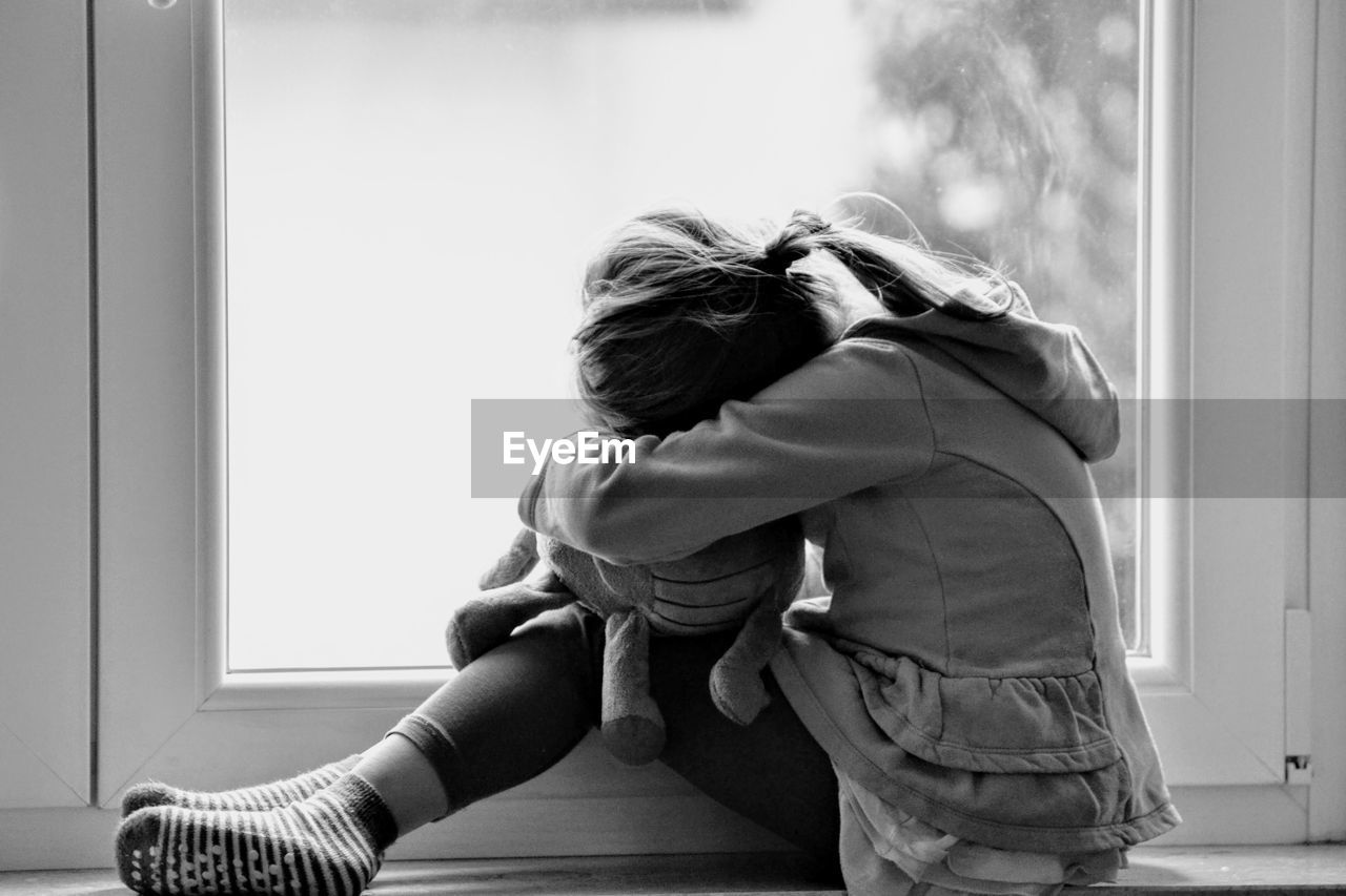 Side view of depressed girl sitting on floor at home