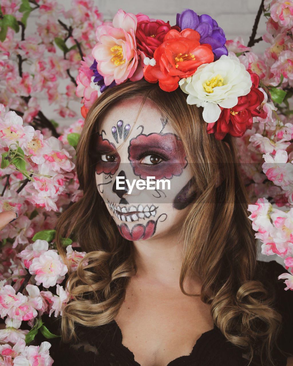 PORTRAIT OF WOMAN WITH PINK FLOWERS IN FRONT OF RED FLOWERING PLANT