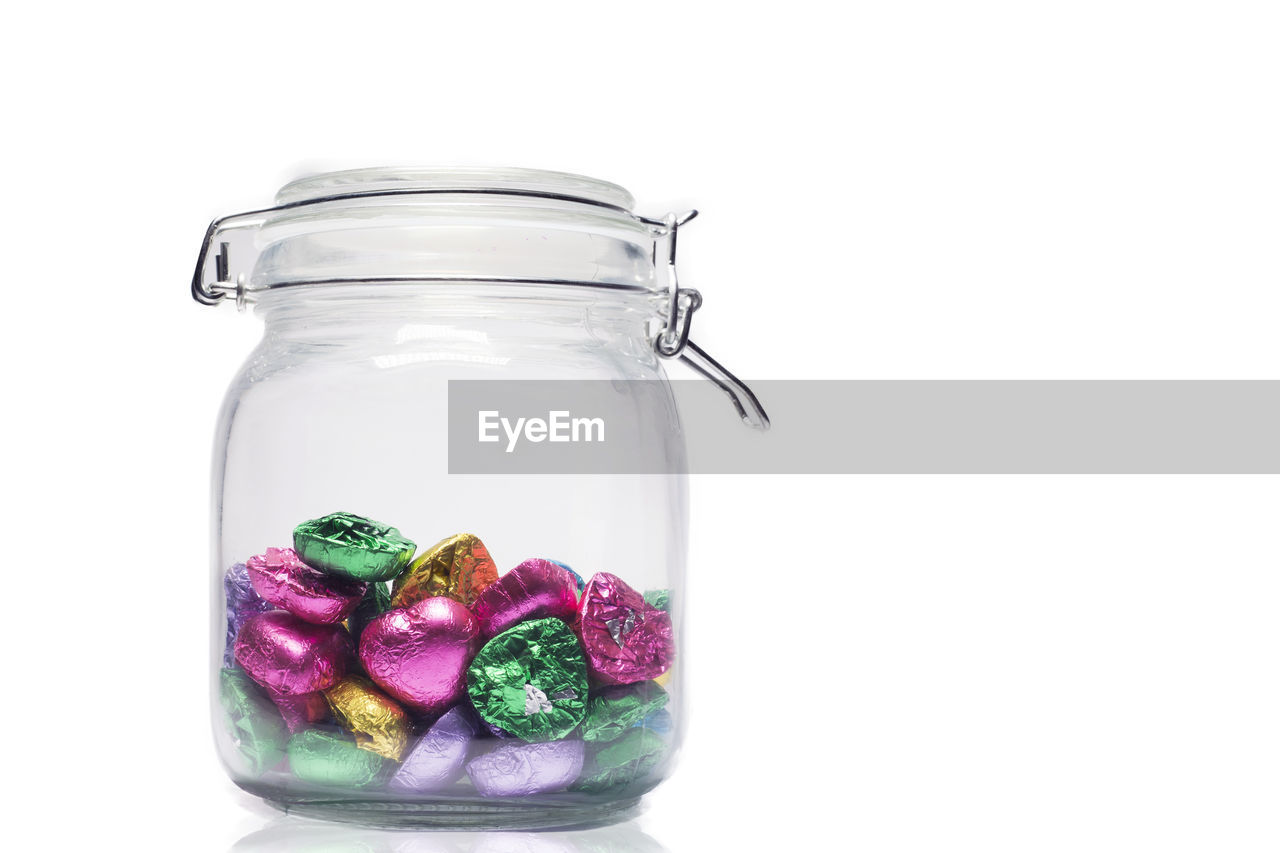 Close-up of wrapped chocolates in jar against white background