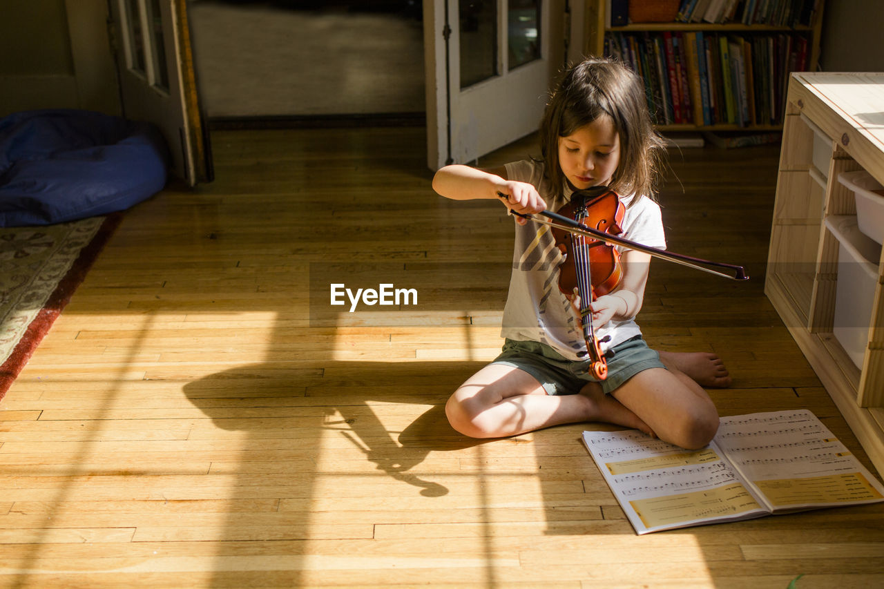 A small girl sits on floor playing violin in front of open music book