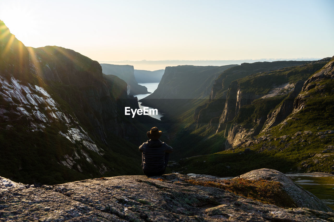 Rear view of man looking at mountains view while sitting against sky