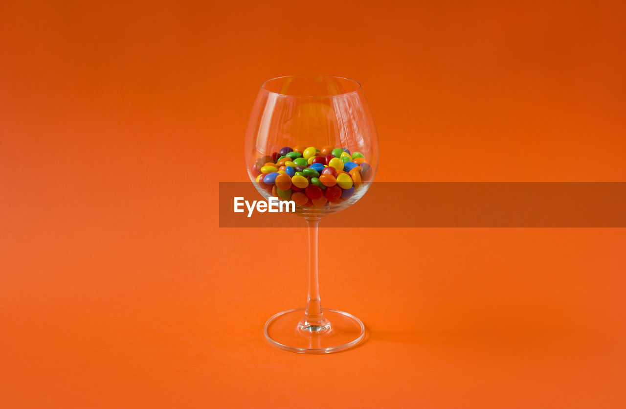 Colorful candies in a wine glass on the orange colored background, minimalism