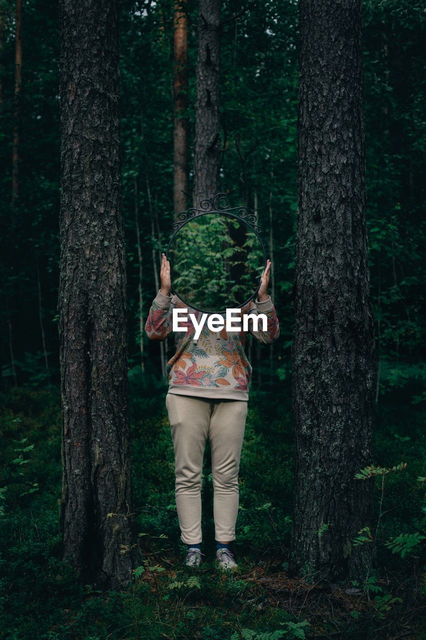 Woman standing by tree trunk in forest