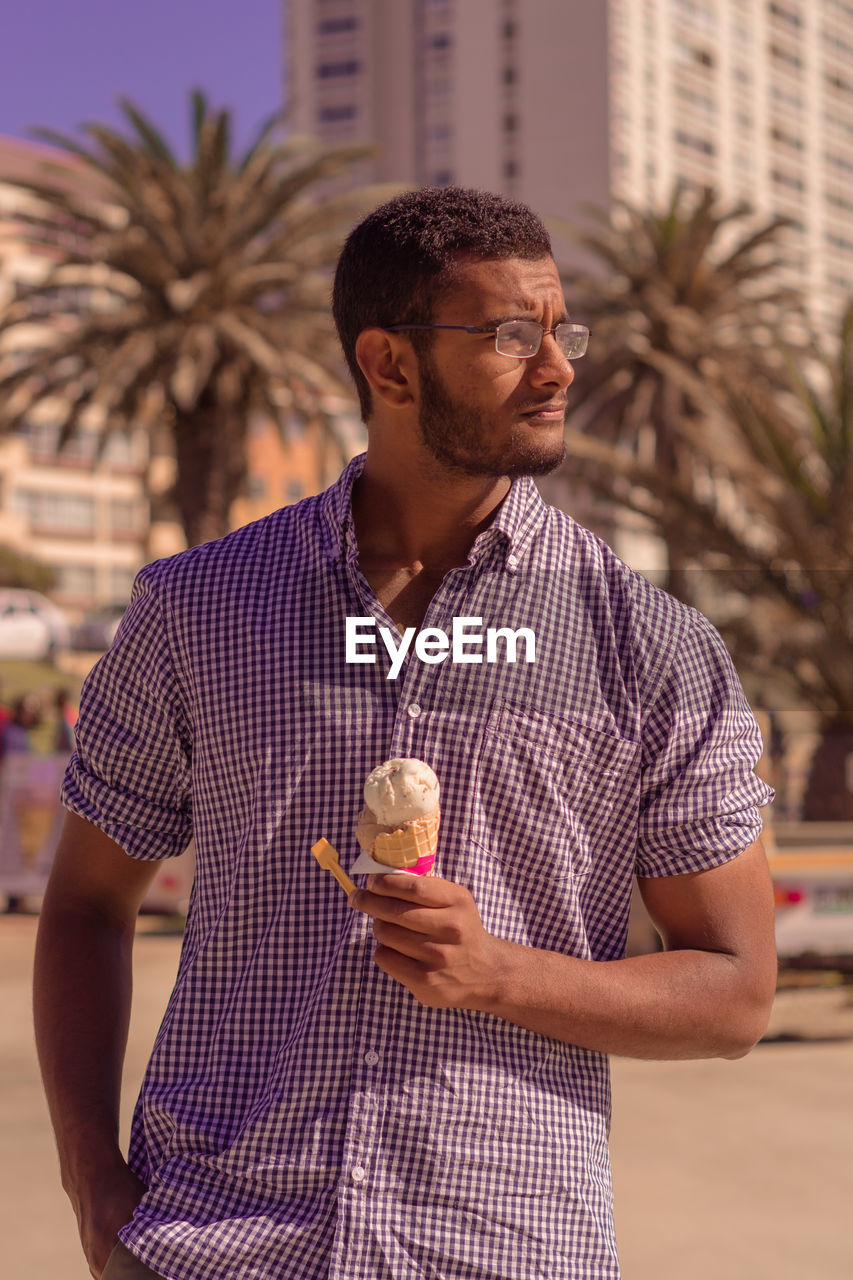Man with ice cream looking away while standing at beach