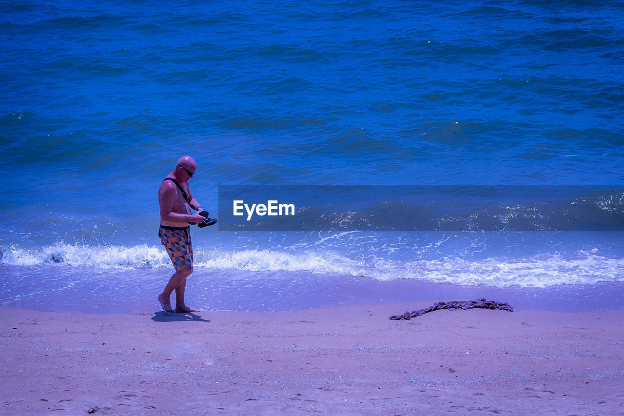 REAR VIEW OF WOMAN STANDING ON BEACH