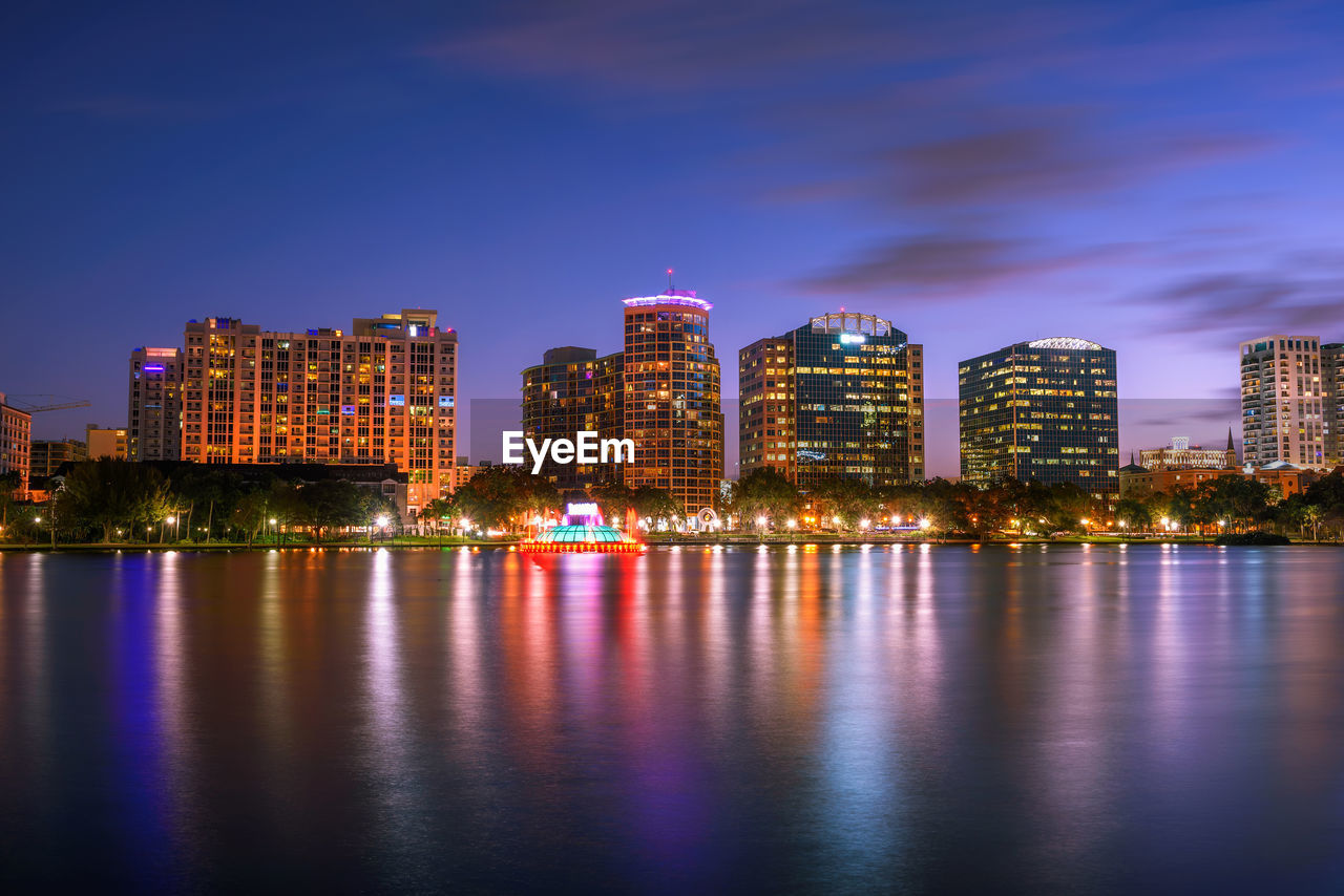 ILLUMINATED CITY BY RIVER AGAINST SKY AT NIGHT