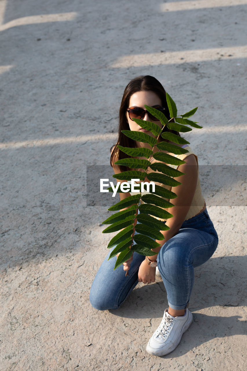 Portrait of young woman in sunglasses holding plant outdoors