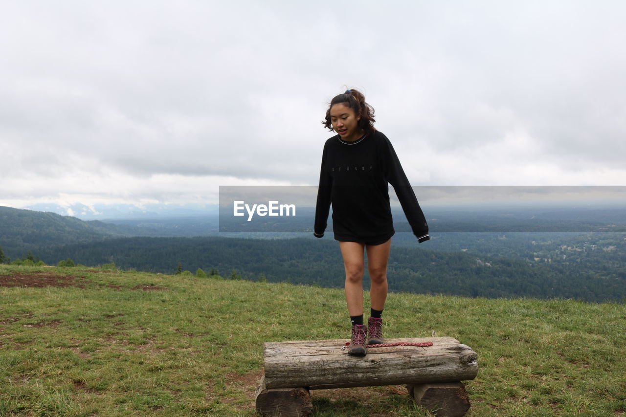 Woman walking on bench over landscape against sky