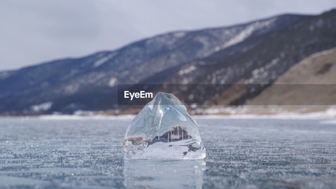 CLOSE-UP OF ICE CRYSTALS ON SHORE AGAINST MOUNTAIN