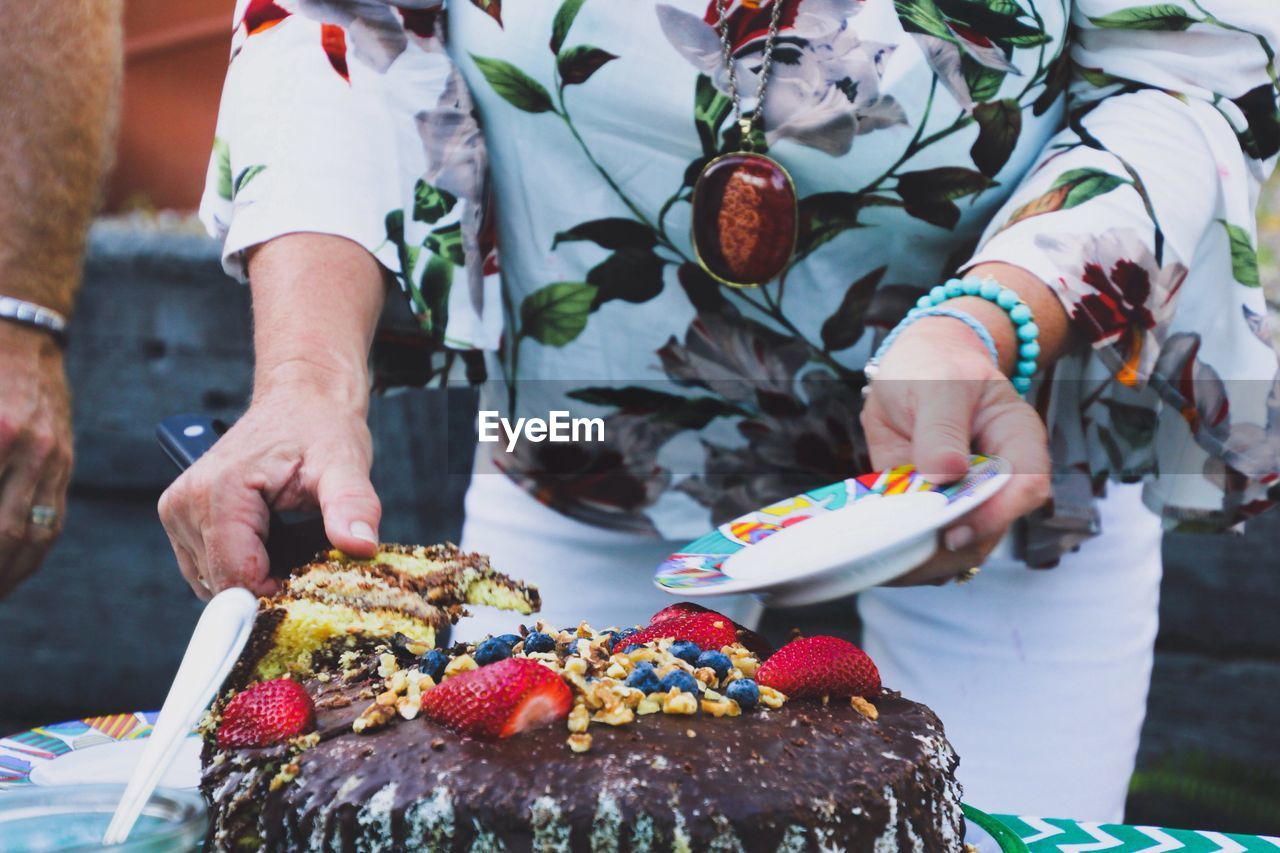 Midsection of woman cutting birthday cake on table