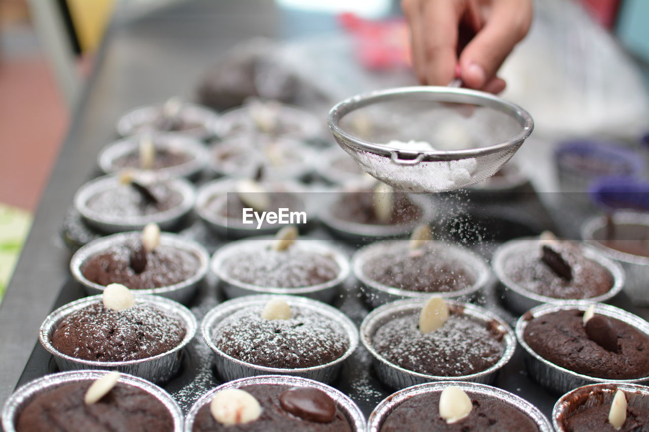 Close-up of hand sprinkling powdered sugar in muffins