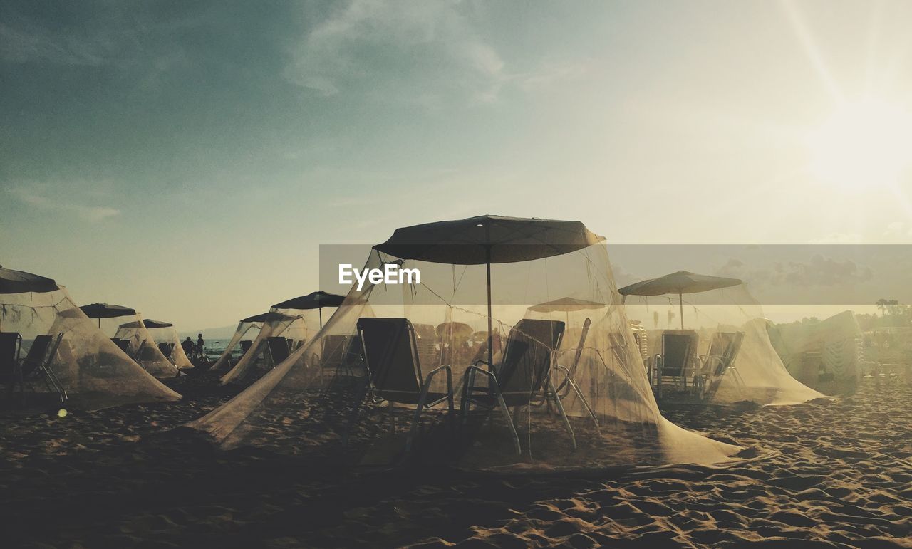 Chairs and parasols covered with mosquito nettings at beach against sky