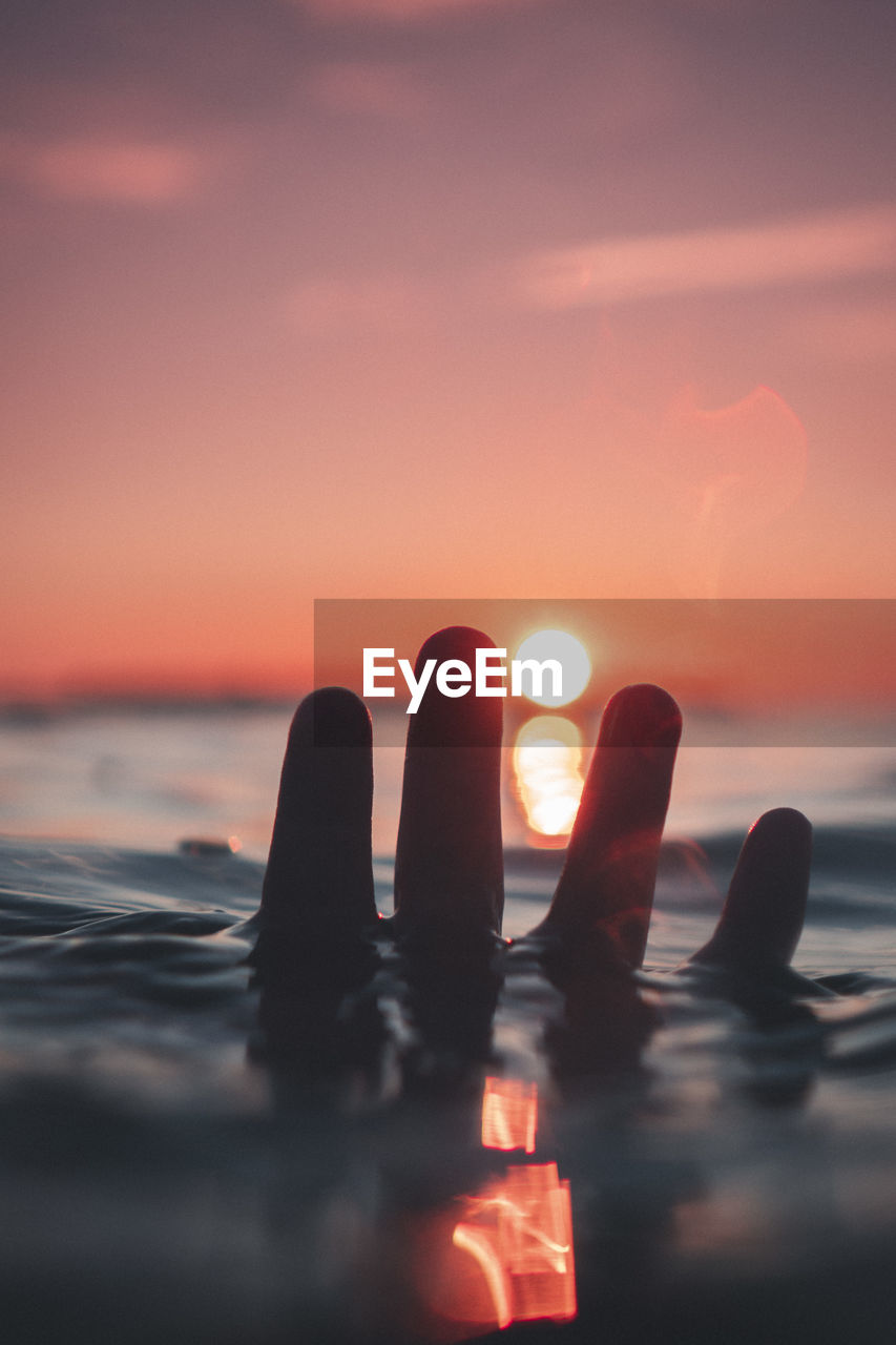 Male human hand in the water longing for the sunset
