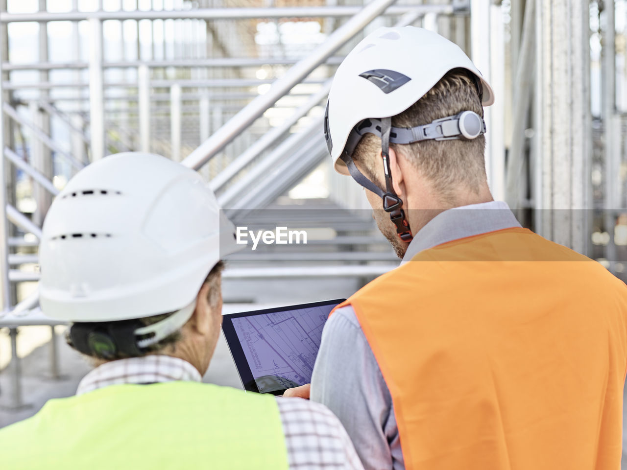 Architect and foreman with tablet wearing hards hat on construction site