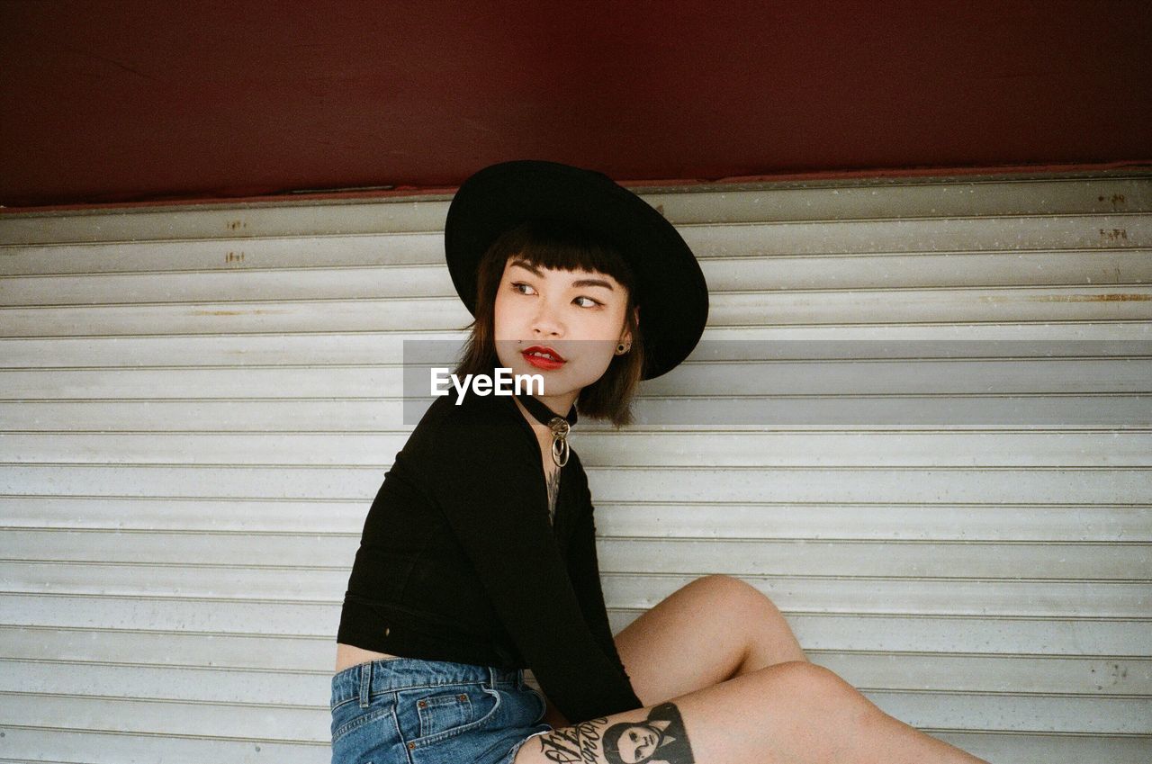 Young woman looking away while sitting by wall