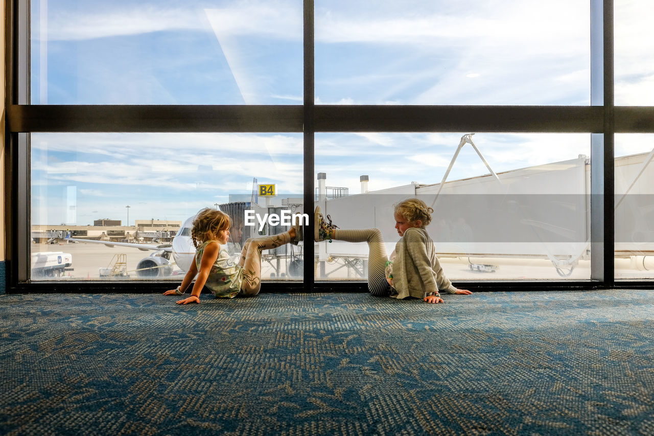 Little girls sitting on ground looking in airport terminal