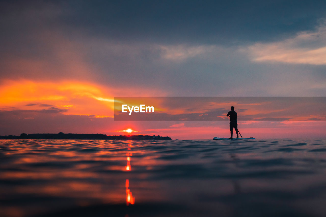 Silhouette man standing on paddleboard against sky during sunset