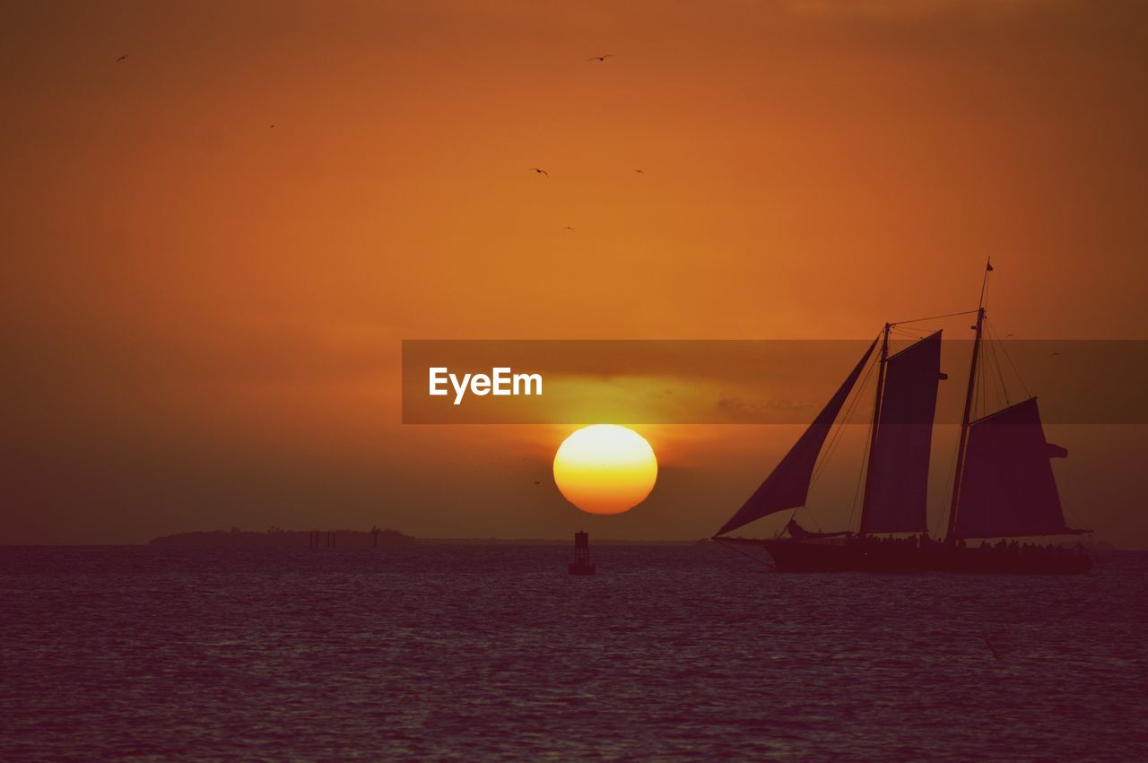 Silhouette sailboat in sea against orange sky