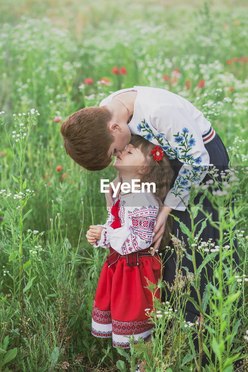 Mom in ukrainian national dress kisses her daughter in a field with flowers
