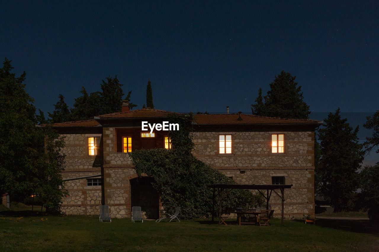 HOUSE BY ILLUMINATED TREES AGAINST SKY AT NIGHT