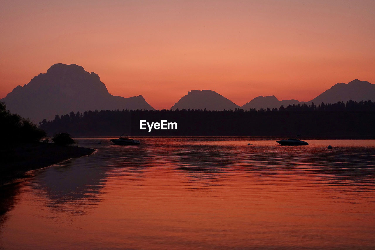 Scenic view of lake by silhouette mountains against sky during sunset