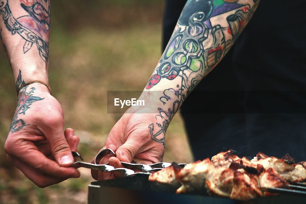 Tattooed hands grilling meat