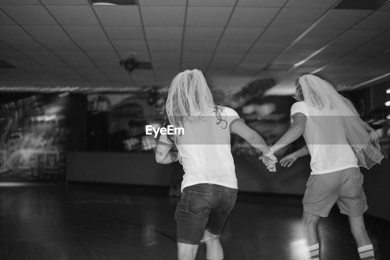 REAR VIEW OF TWO WOMEN STANDING ON FLOOR IN CORRIDOR