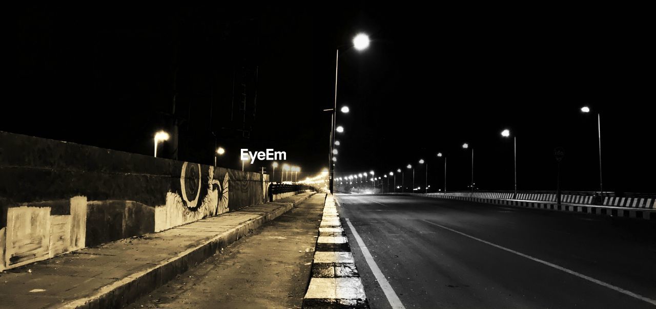 EMPTY ROAD ALONG ILLUMINATED STREET LIGHTS IN CITY AT NIGHT