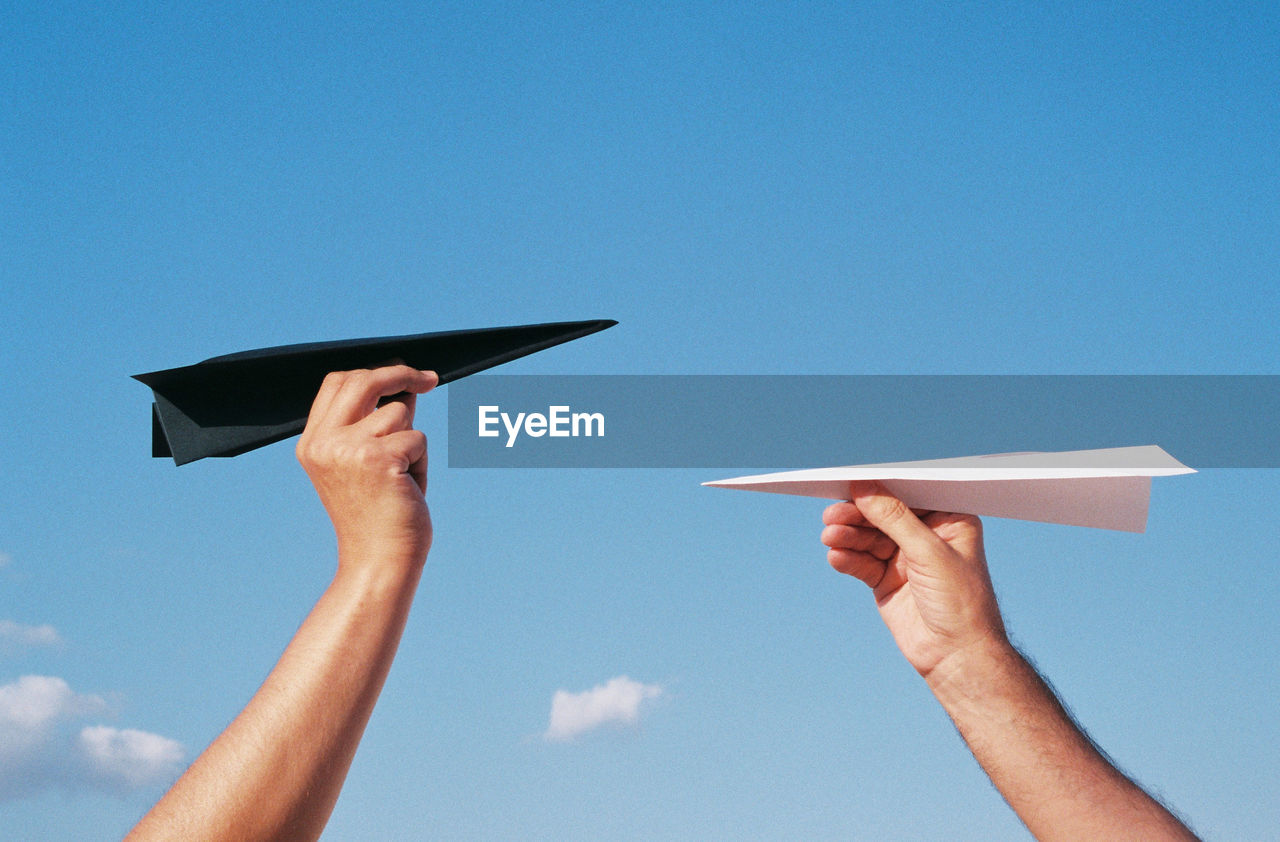 Low angle view of person hand with paper plane against blue sky