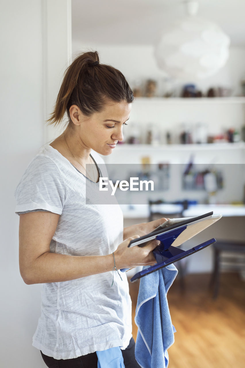 Woman using digital tablet while holding squeegee at home