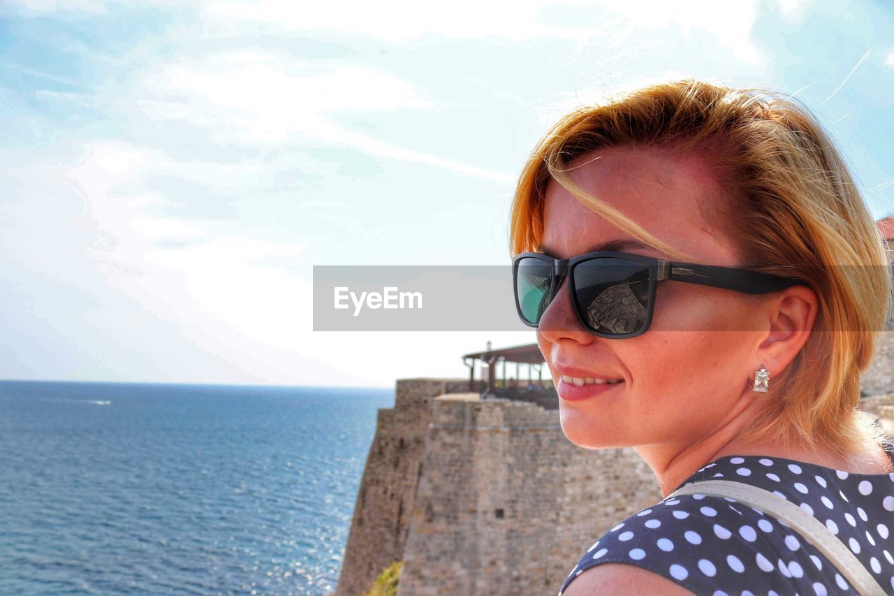 Close-up of smiling young woman looking away against sea