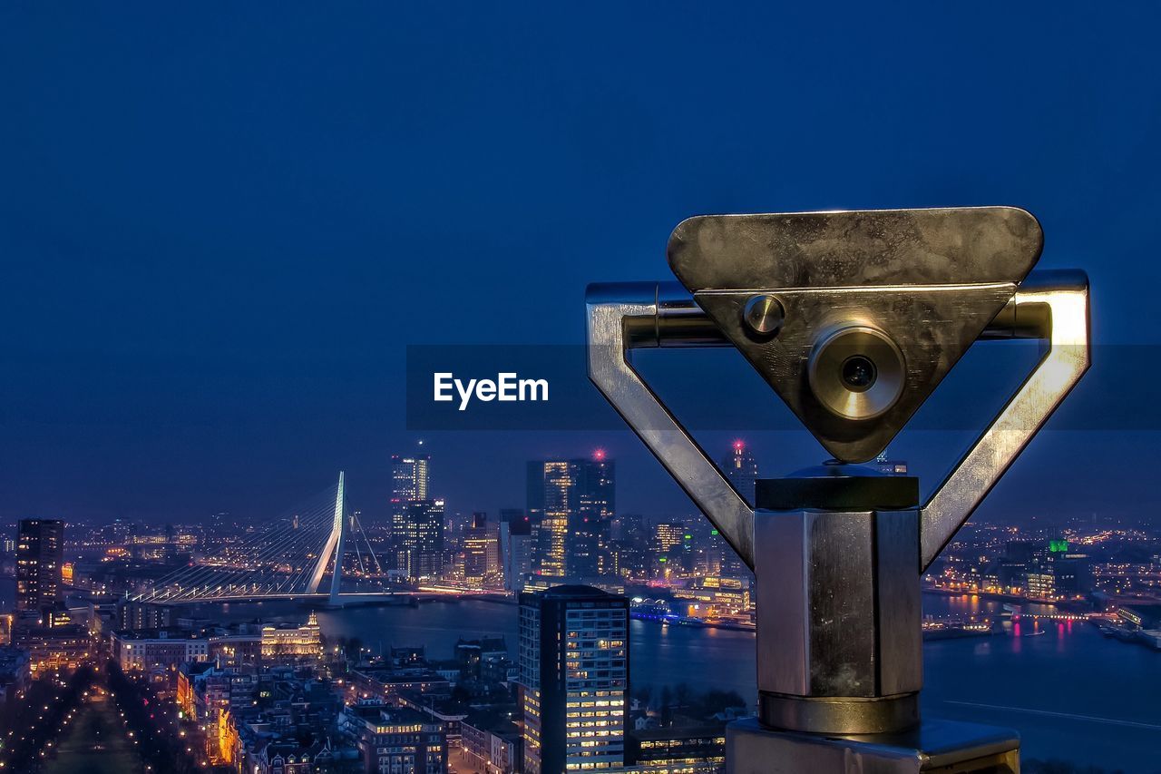 Coin-operated binocular by illuminated cityscape against sky at dusk