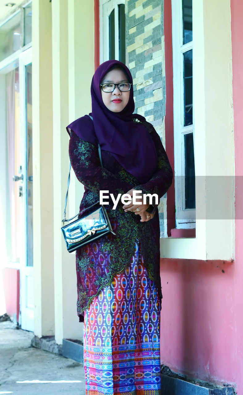 Portrait of a young woman wearing a hijab posing with glasses and wearing traditional indonesian