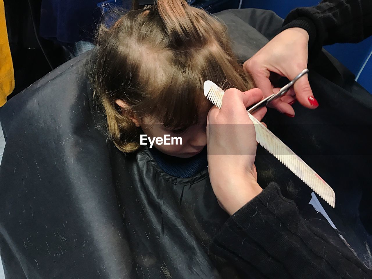 Cropped hands of barber cutting girl hair