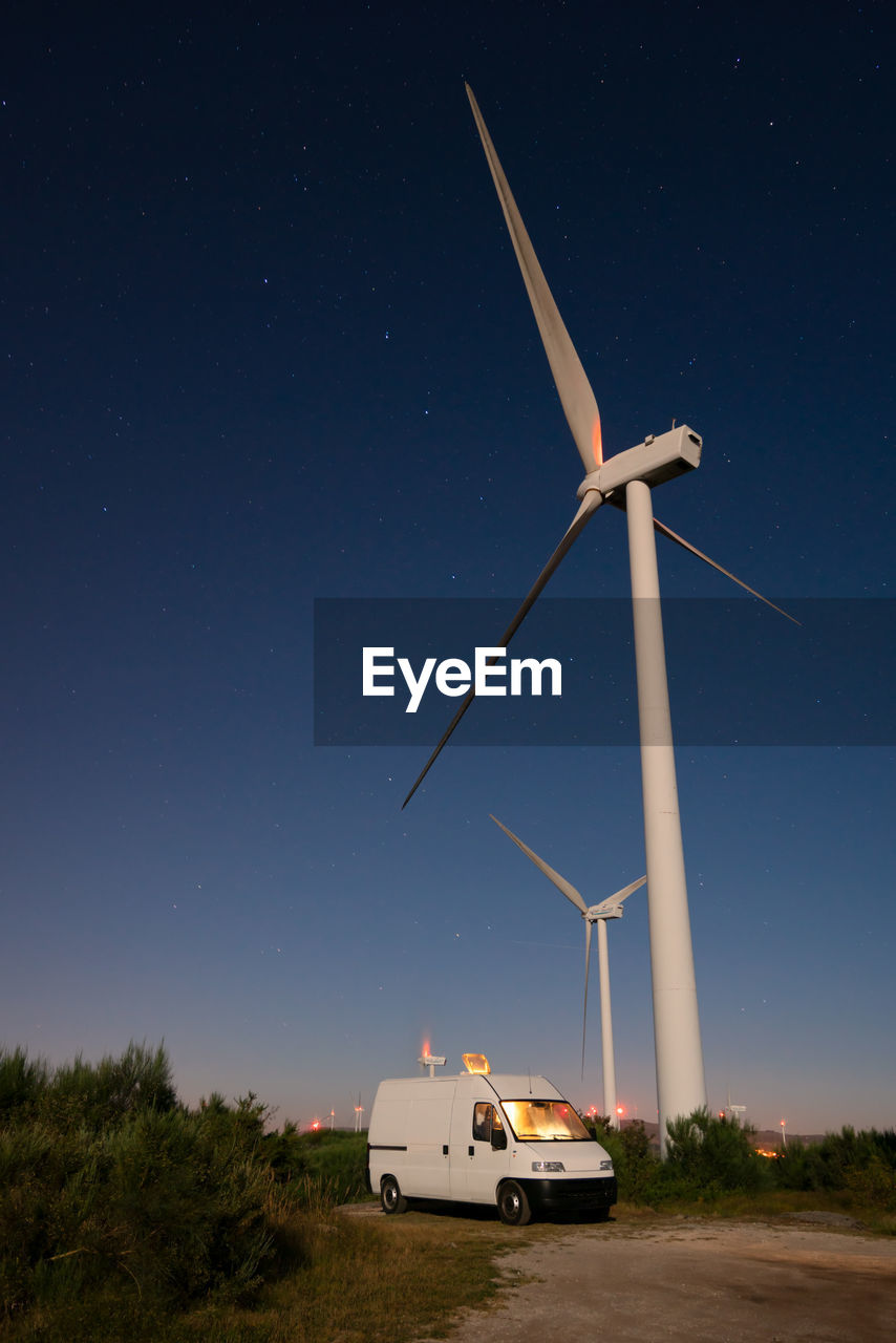 Camper van van life social distancing near a wind eolic turbine at night with stars on the sky