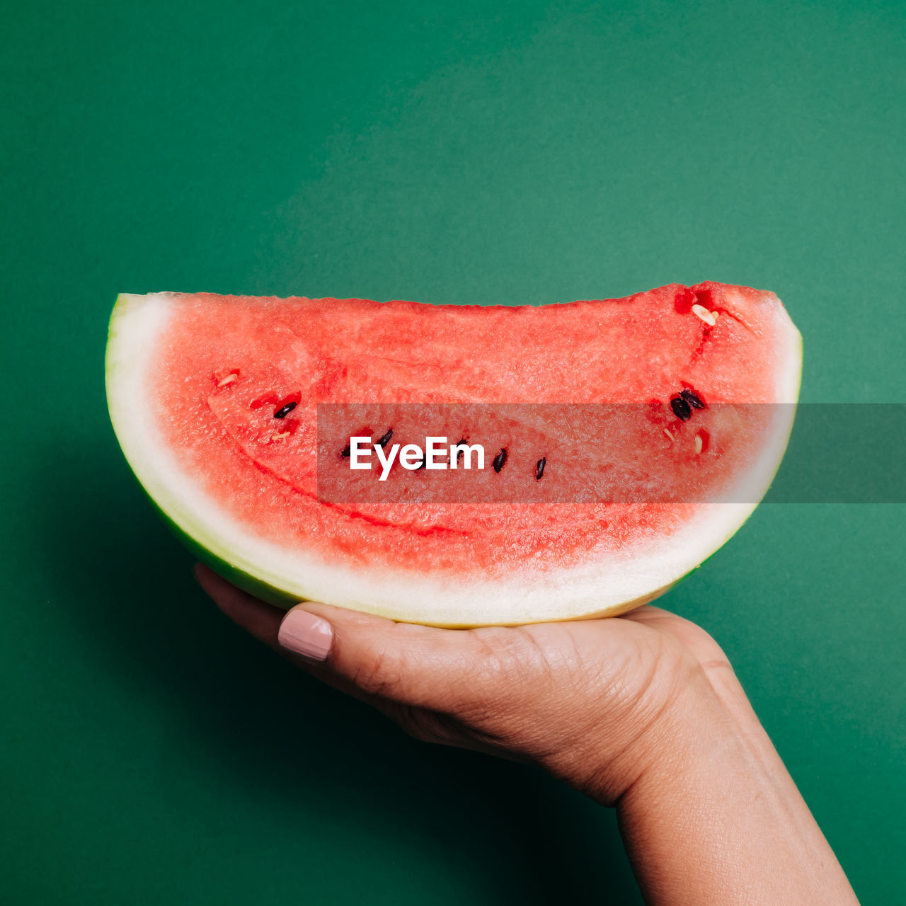 Close-up of hand holding watermelon against green background