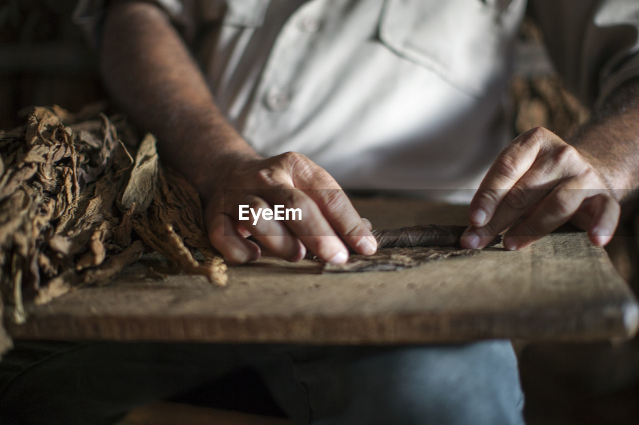 Midsection of man rolling dry leaves on table at workshop