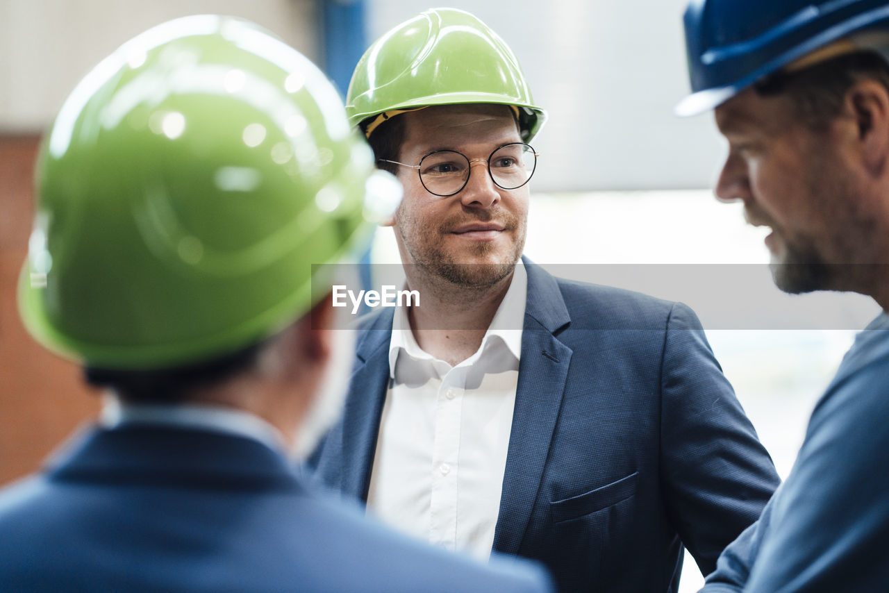 Male professionals looking at coworker discussing at warehouse