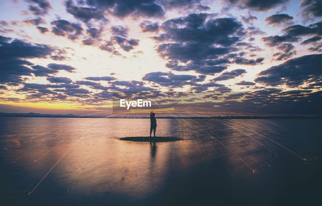 SILHOUETTE MAN STANDING ON SEA AGAINST SKY DURING SUNSET