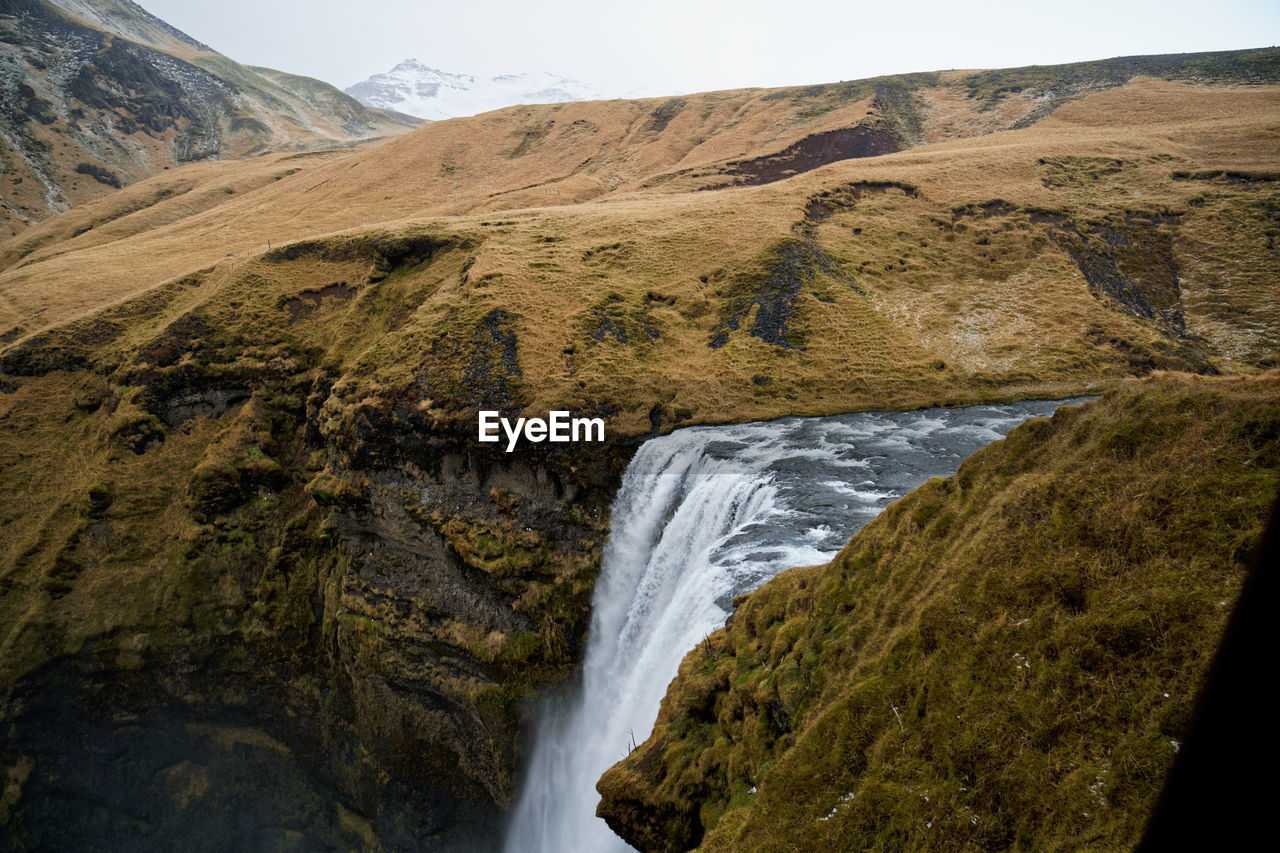 SCENIC VIEW OF WATERFALL AGAINST ROCKY MOUNTAINS