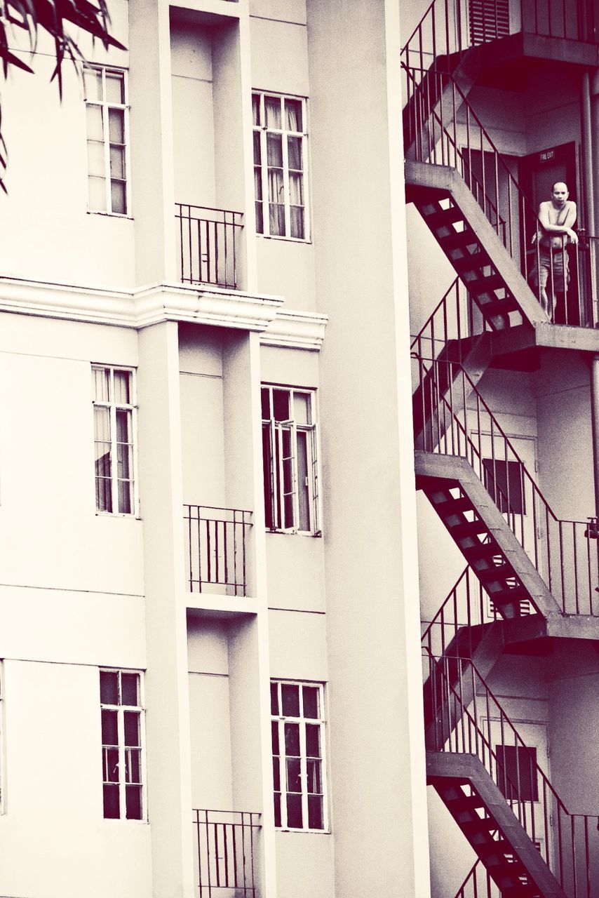 Shirtless man standing on fire escape steps of building