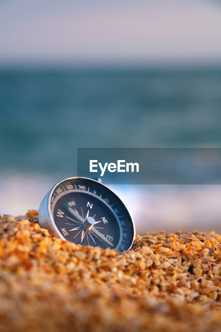 Conceptual photo, close-up of a compass lying in wet sand consisting of small crumbs of shells