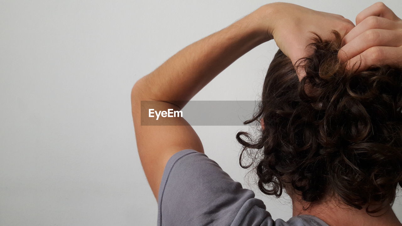Rear view of woman tying hair against white background