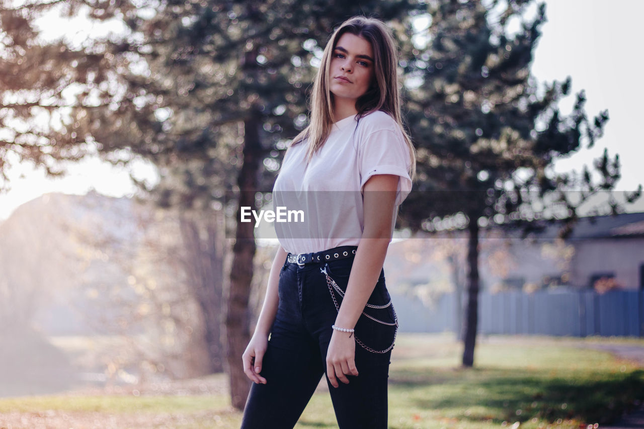 Portrait of young woman standing against trees