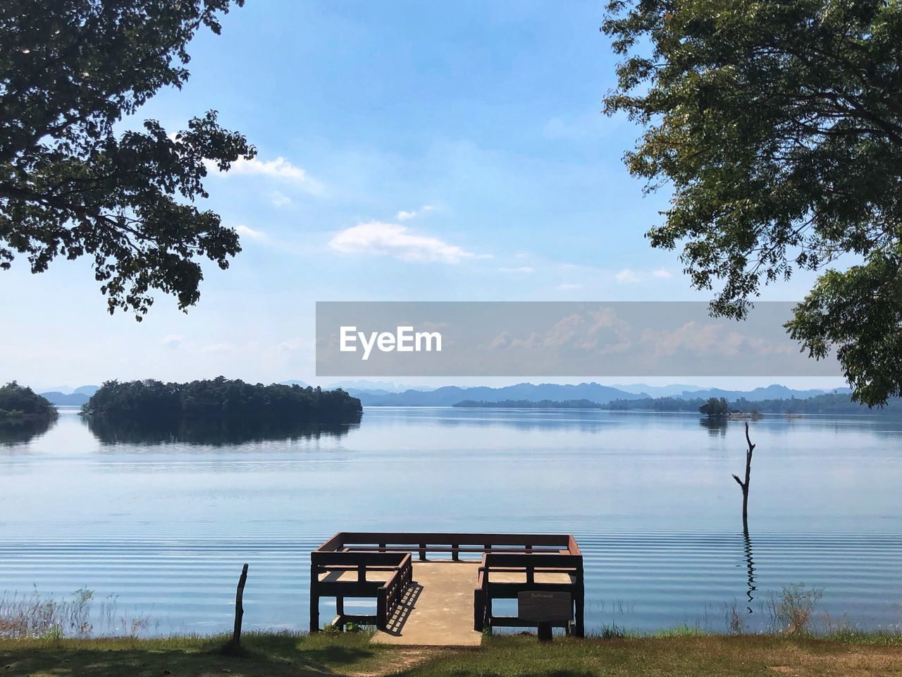 Empty bench by lake against sky