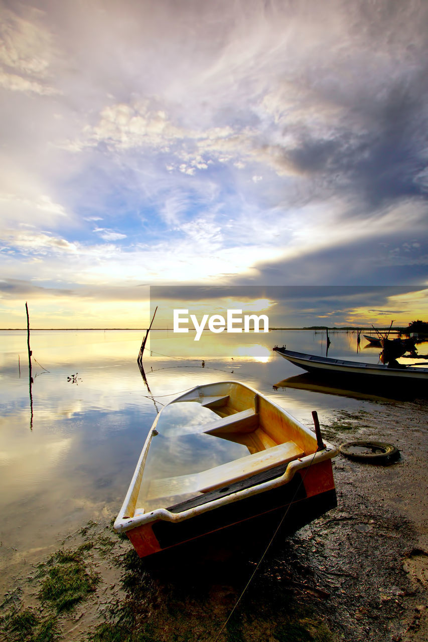 Boat moored on beach against sky during sunset