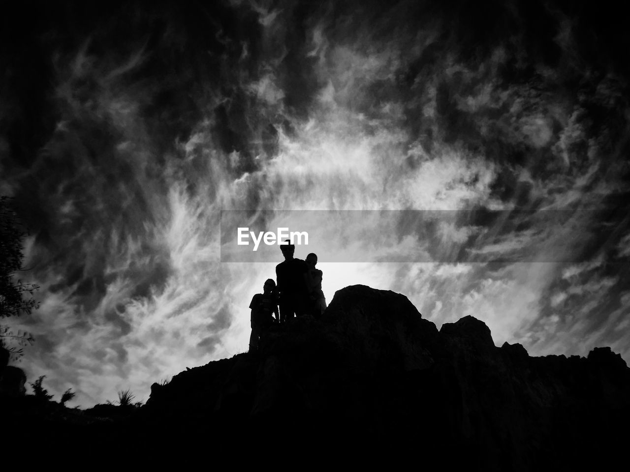 Low angle view of silhouette people on rock formation against cloudy sky